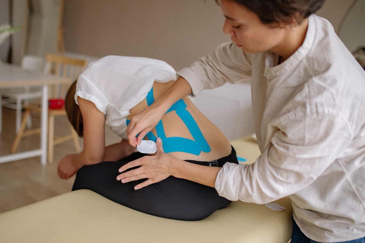 A practitioner applying kinesiology tape to a patient's lower back